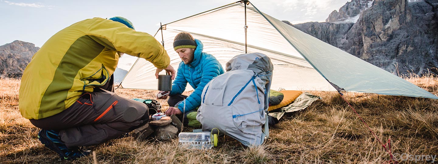 two people sitting under a lightweight tarp with a cooking stove
